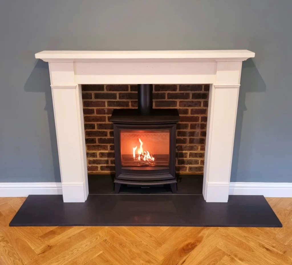 A white surround with a brick-lined opening, black stove and parquet floor.