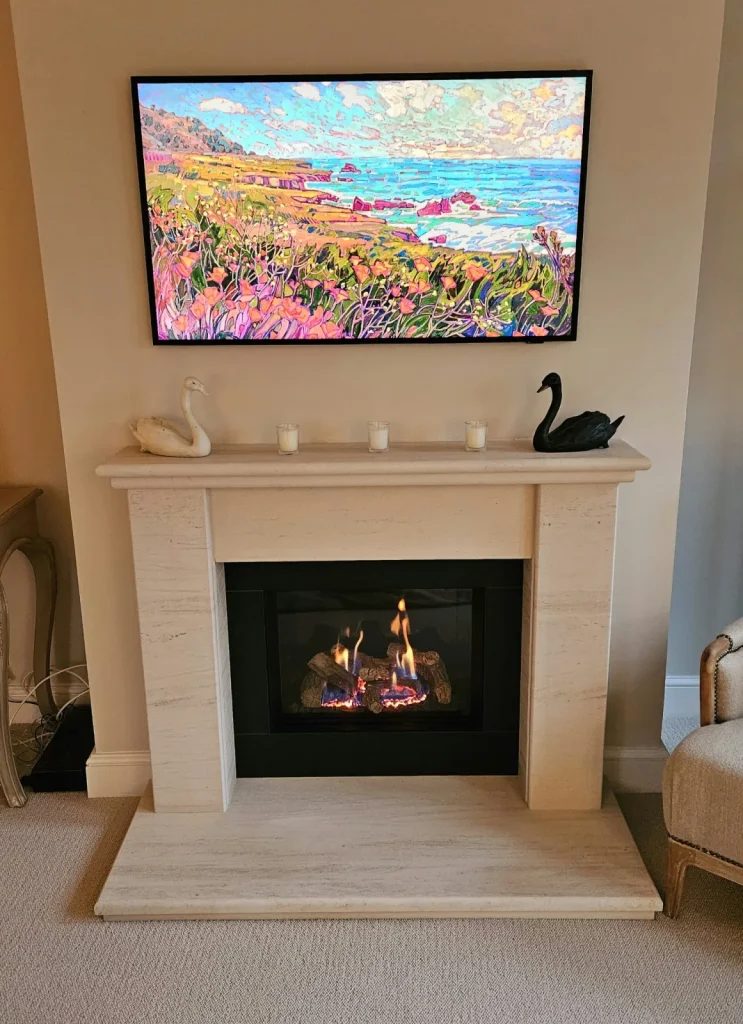 A pale traditional surround and lit inset fire below a television in a furnished living room.